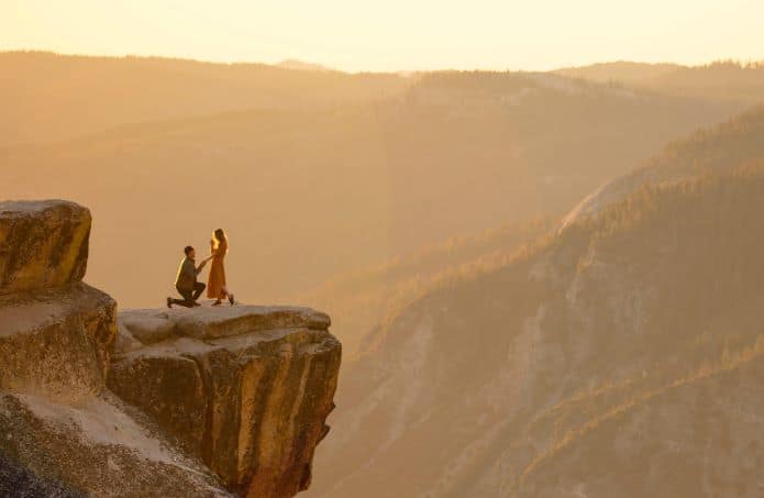 homme à genoux devant une femme sur un rocher au loin