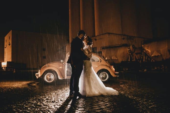 couple de mariés détendu devant une voiture sous la pluie